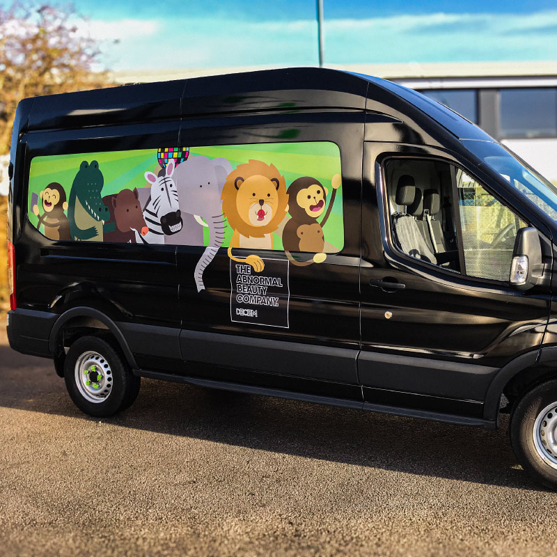 A black van with a panel graphic featuring cartoon animals and the logo for 'Deciem' with their slogan 'The abnormal beauty company'