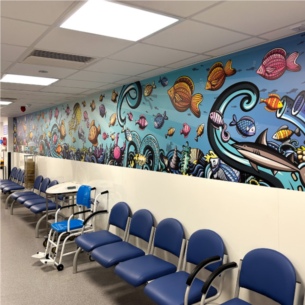 A long hallway with chairs down the side for waiting. The top half of the room has a underwater print vinyl.