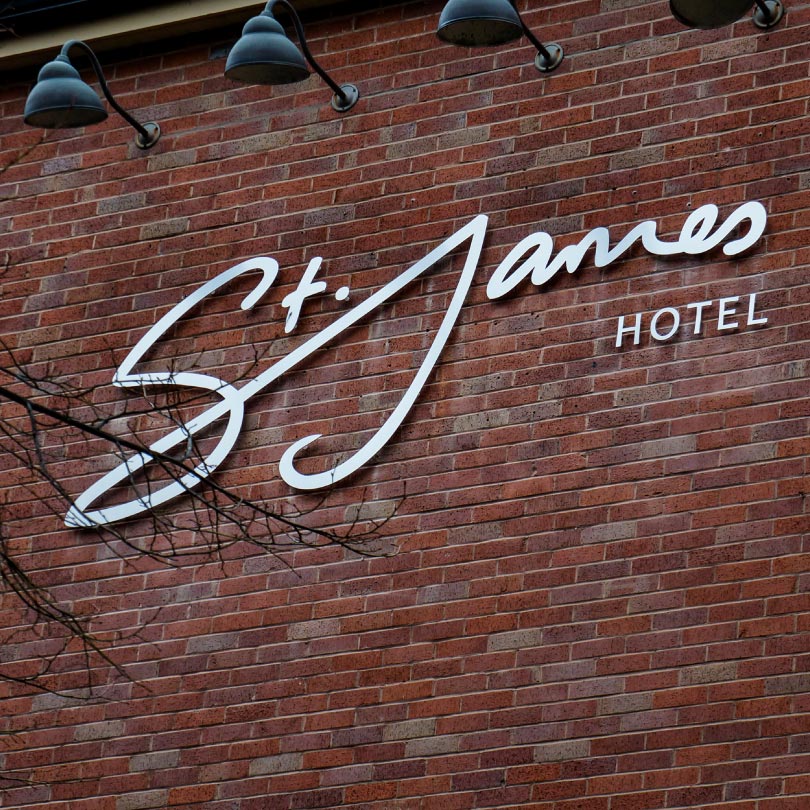 The Image shows a brick wall with a St. James written in large script lettering with hotel written next to it in a san-serif font.